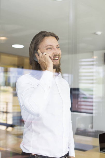 Boldog fiatalember használ a szúró telefon, modern irodában - Fotó, kép