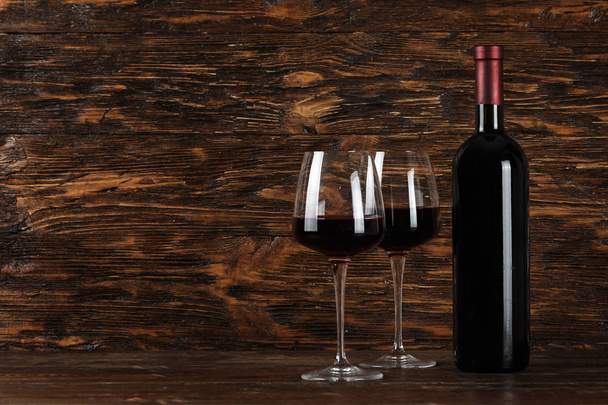 bottle of red wine and a glass of wine on a wooden background. without labels. space for tex - Фото, изображение