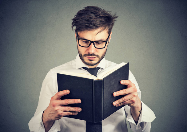 Young man in glasses reading a smart book on gray background - Photo, image