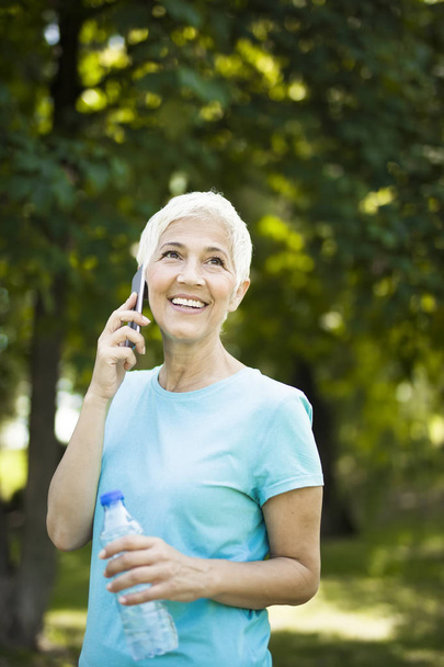 Portrait of sporty senior woman using mobile phone in the park - Foto, imagen
