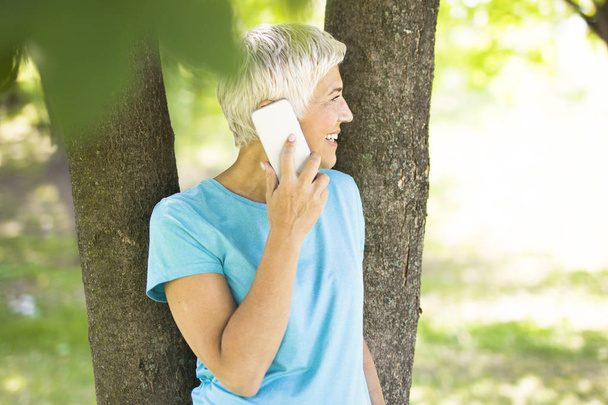 Muotokuva urheilullinen vanhempi nainen käyttää matkapuhelinta puistossa
 - Valokuva, kuva