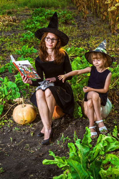Mãe e filha em trajes de uma bruxa estão sentados em abóboras e lendo um livro, conceito de Halloween. A família está se preparando para o feriado Halloween. Halloween fundo, espaço livre
. - Foto, Imagem