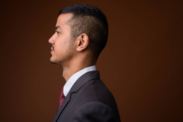 Plan studio d'un jeune homme d'affaires asiatique multi-ethnique portant un costume sur fond brun
 - Photo, image