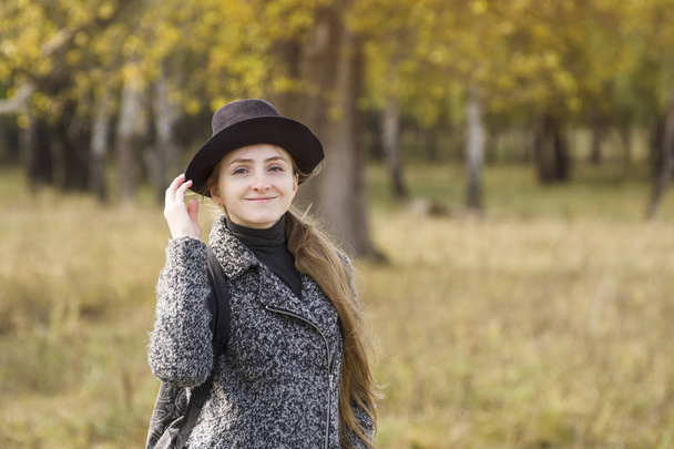 Smiling girl in a hat standing in the autumn forest. Back view - Zdjęcie, obraz