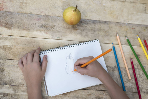 Детские руки рисуют грушу цветными карандашами. Вид сверху
 - Фото, изображение