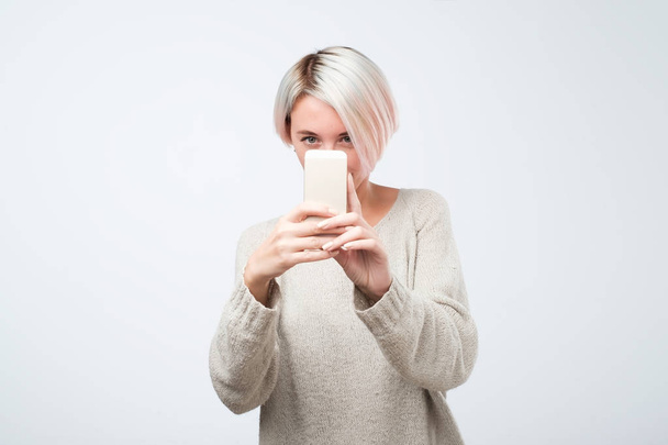 Mujer europea joven con el pelo corto teñido está tomando una foto en un teléfono inteligente
 - Foto, Imagen