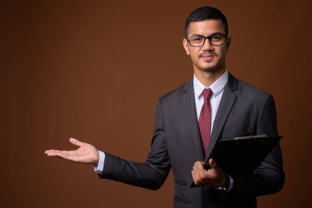 Young multi-ethnic Asian businessman against brown background - Fotografie, Obrázek
