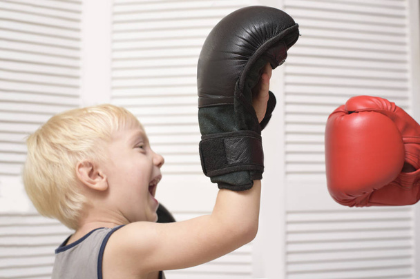 Ξανθό αγόρι πυγμαχία με το χέρι σε κόκκινο γάντι. Συναισθήματα - Φωτογραφία, εικόνα