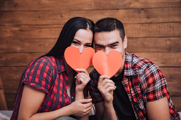 couple in love close their faces with paper hearts on Valentine's Day. Idea for a photoshoot for lovers - Photo, image