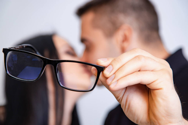 man shows modern eyeglasses and kisses on the background of his girl and himself. Close-up - 写真・画像