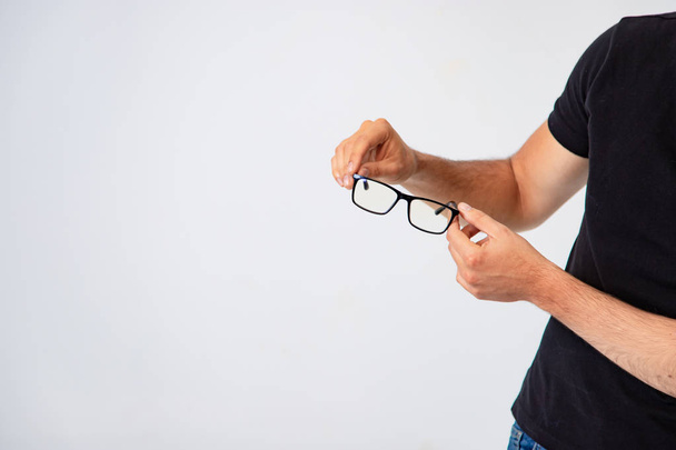fashionable glasses with a black frame are in the hands of a man on a white background in the studio. Adult man is dressed in black t-shirt. Close-up - Foto, Imagem