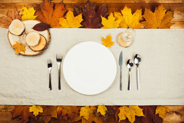 Прекрасный вид на осенний декор и столовые приборы на деревянном столе подается на праздничный ужин. Осень кленовые желтые и красные листья
 - Фото, изображение