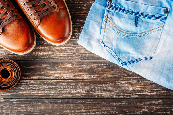 Herrenstiefel aus braunem Leder, Gürtel und blaue Jeans auf dunklem Holzgrund, Draufsicht mit Kopierraum - Foto, Bild
