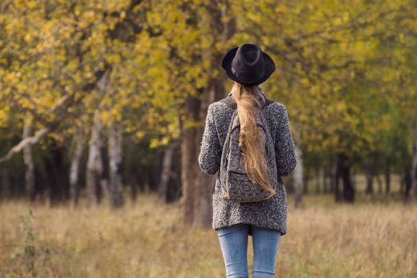 Дівчина в капелюсі з рюкзаком, що стоїть в осінньому лісі. Вид ззаду
 - Фото, зображення