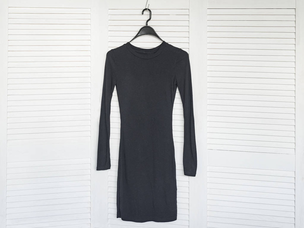 Маленька чорна сукня висить на вішалці. Білий дерев'яний екран на фоні. Модний гардероб
 - Фото, зображення