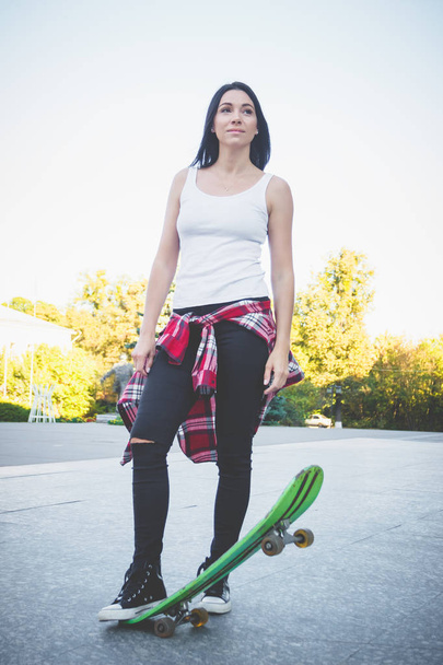 Beautiful woman with a skateboard on the street, soft focus background - Фото, изображение