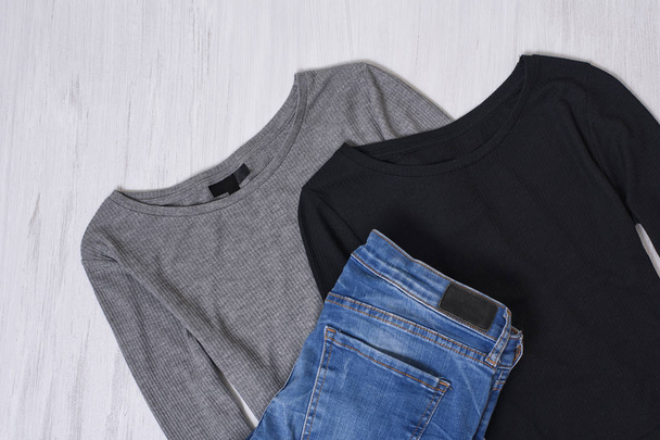 Black and gray tops and jeans on wooden background. Fashionable concept - Zdjęcie, obraz