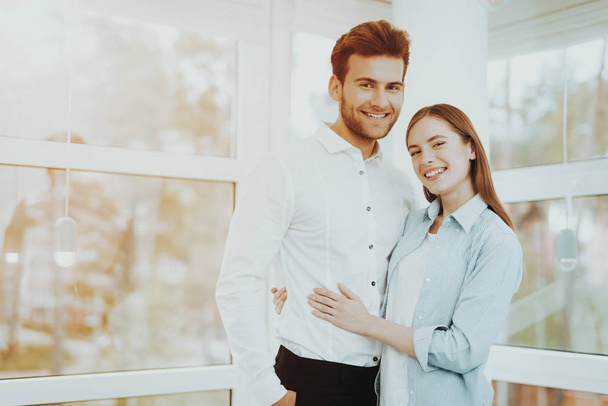 Young Couple Posing In The Bright Room. Buying A Property. Panoramic Windows. Hugging Each Other. Happy Family Relationship. Smiling Together. Sunny Day. Rent A House. Cheerful Sweethearts. - Photo, image