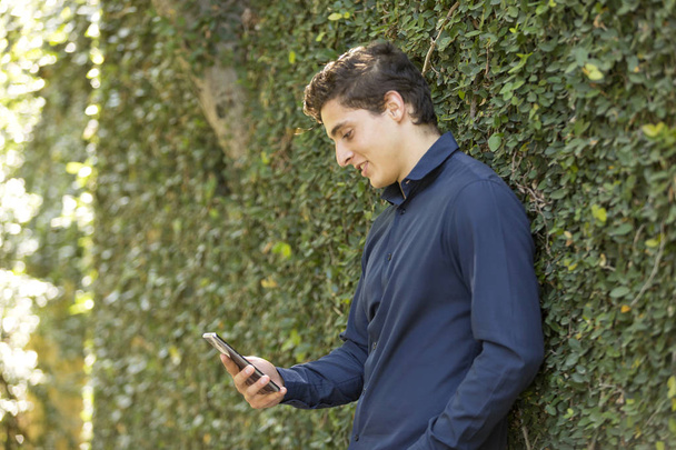 Front view portrait of a young businessman smiling walking towards camera and texting on phone - Photo, image