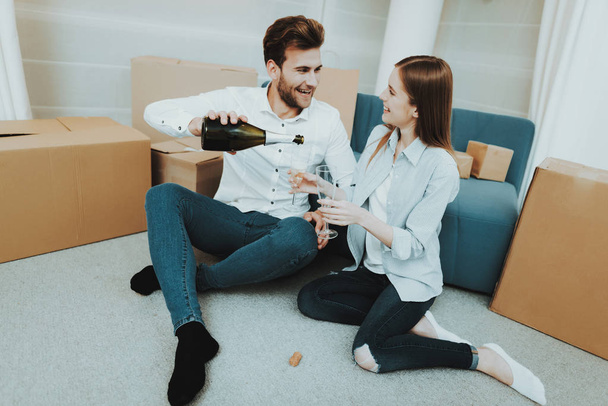 Young Couple In New Apartment. Champagne Celebrating. Love Each Other. Cheerful Sweethearts. New Life. Personal Flat. Happy Family. Domestic Life. Orange Boxes. Siting On The Floor. - Foto, immagini