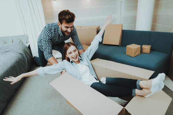 Young Couple Having Fun During Moving Into A New Apartment. Box Rolling Around The House. Holiday Leisure. Happy Family Weekend Joy. Love Each Other. Newlyweds In A New Housing. Relocation In Flat. - Photo, image