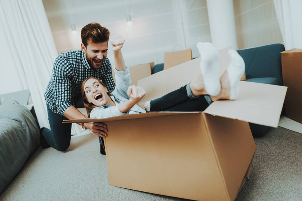 Young Couple Having Fun During Moving Into A New Apartment. Box Rolling Around The House. Holiday Leisure. Happy Family Weekend Joy. Love Each Other. Newlyweds In A New Housing. Relocation In Flat. - Фото, изображение