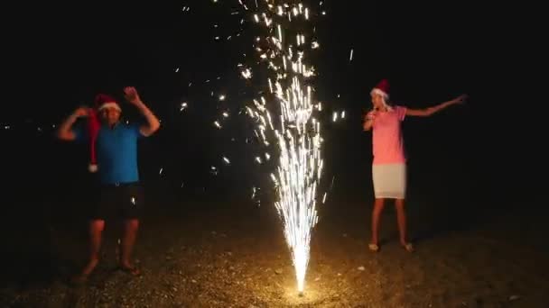 Νεαρός άνδρας και γυναίκα στο Χριστούγεννα καπέλα runnig πυροτεχνήματα Κρήνη σπινθήρες γύρω από - Πλάνα, βίντεο