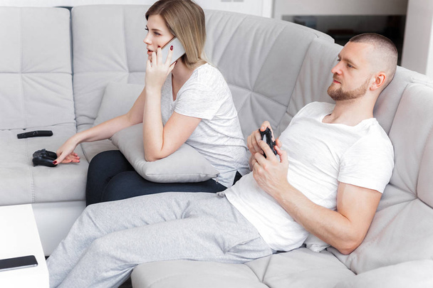 Man playing TV console. Woman using phone. Family weekend relax home on sofa - Photo, Image