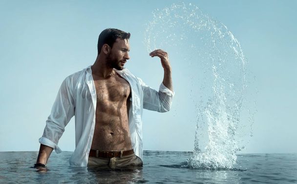 beau homme brutal en blanc mouillé court éclabousse l'eau autour de lui sur une plage ou une piscine se sentant en bonne santé, en forme et libre
 - Photo, image