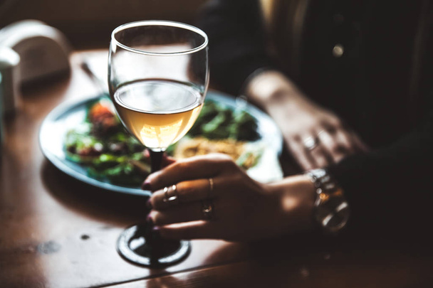 Женская рука с бокалом вина и едой на заднем плане
 - Фото, изображение