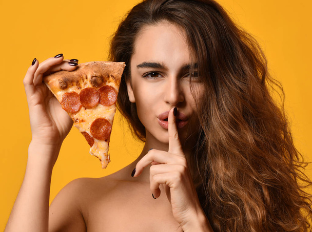 Young beautiful woman hold slice of pepperoni pizza and show tss quite sing on yellow - Φωτογραφία, εικόνα