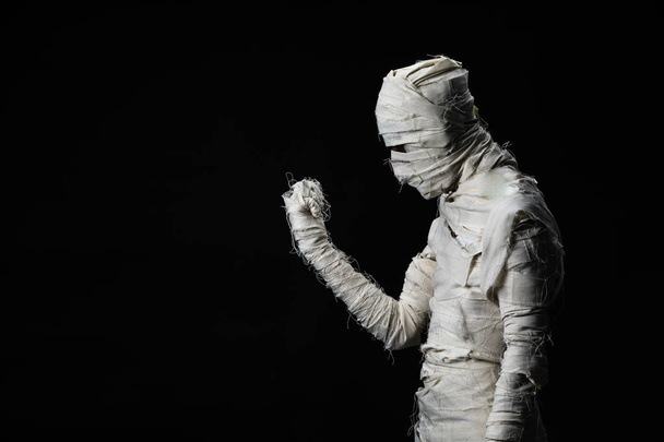 Estúdio tiro retrato de jovem em traje vestido como um cosplay halloween de mummy assustador pose como um olhar para a mão direita agindo sobre fundo preto isolado
. - Foto, Imagem
