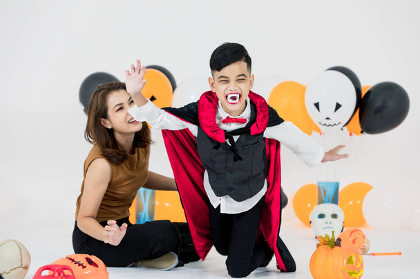 Studio strzał matka rodziny pomoc dziecko w stroju przebrany cosplay halloween przerażające Draculi w pokoju wypełnionym balony na białym tle. - Zdjęcie, obraz