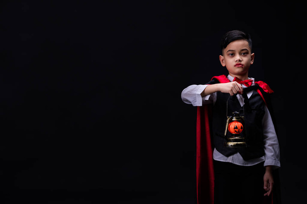 Estúdio tiro retrato de menino em traje vestido como um cosplay halloween de dacula assustador segurando uma lanterna de abóbora jack 'O isolado no fundo preto
. - Foto, Imagem