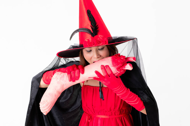 Studio βολή της γυναίκας στο κόκκινο κοστούμι κρατώντας ψεύτικο ανθρώπινο πόδι ψάχνει τρόπο. Έννοια για αστείο δραστηριότητα σε Απόκριες Φεστιβάλ. - Φωτογραφία, εικόνα