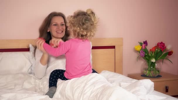 Onnellinen äiti ja pieni tytär istuu sängyllä ja leikkii
 - Materiaali, video