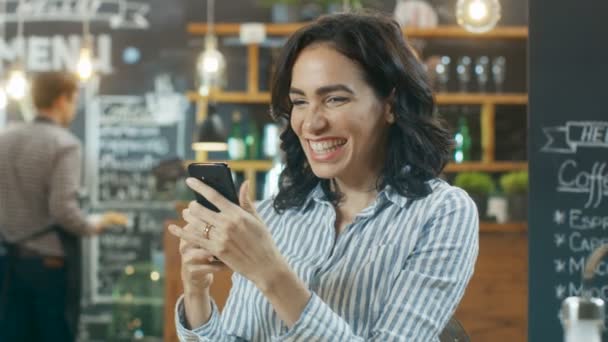 Krásná žena sedí v kavárně. Učí se dobré zprávy z jejího Smartphone a dělá "Ano" gesto. Je nádherná a šťastný. V pozadí stylová kavárna. - Záběry, video