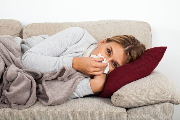 Mujer enferma acostada en el sofá sonándose la nariz - infección sinusal
 - Foto, imagen