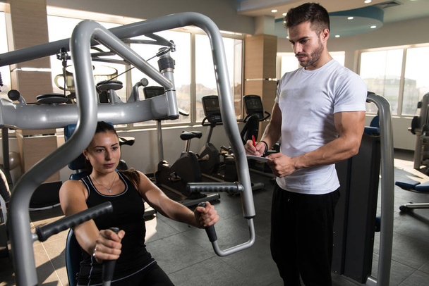Personal Trainer Showing Young Woman How To Train Chest In The Gym - Foto, Imagen