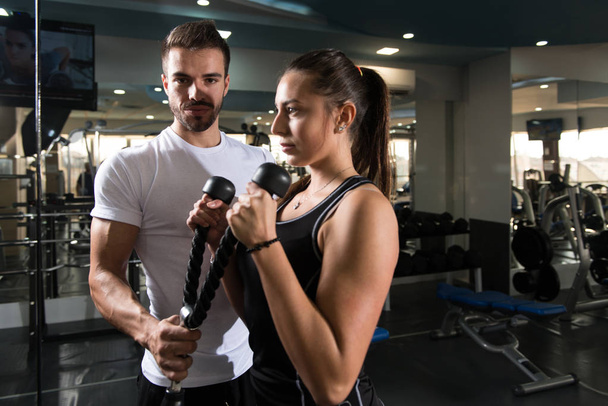 Personal Trainer Showing Young Woman How To Train Biceps In The Gym - 写真・画像