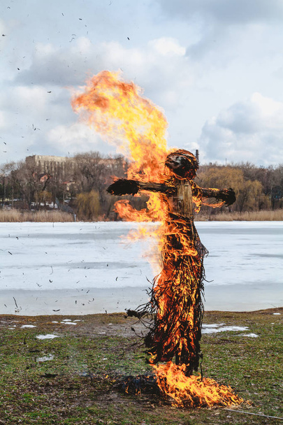 Vacaciones eslavas de fin de invierno. Una gran muñeca Shrovetide de paja arde en la orilla del río. El humo negro es visible
 - Foto, Imagen
