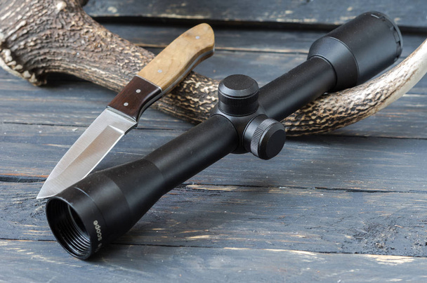 Optical sight and hunting knife. Dark wooden background. Hunter accessories. - Photo, Image