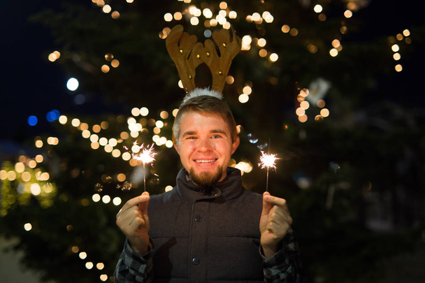 Boże Narodzenie, ludzi i zimowe wakacje koncepcja - zaskoczony mężczyzna w rogi jelenie stojący w nocy ulica bengal światła w jego rękach - Zdjęcie, obraz