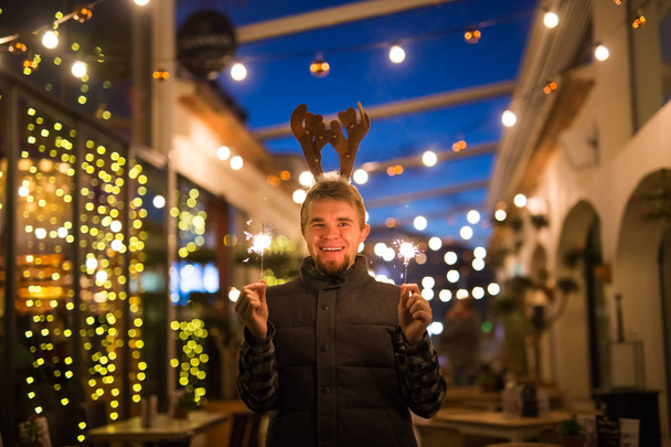 Persone, vacanze e concetto di Natale - giovane uomo divertente in costume da cervo natalizio con luce bengala all'aperto
 - Foto, immagini