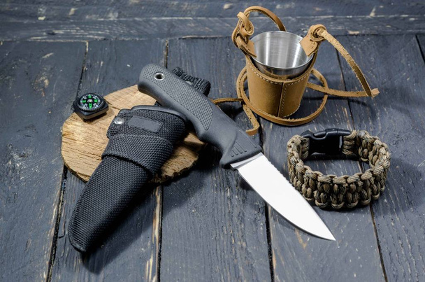 Een militair mes, een survival armband en een metalen glas in de huid. Militaire en jacht. - Foto, afbeelding