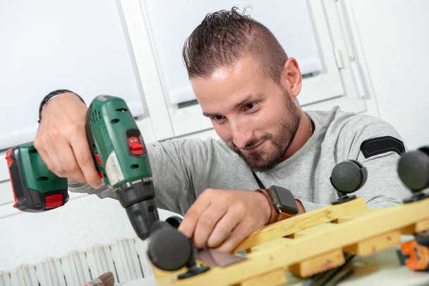 a young handyman  using electric drill, DIY at home  - Foto, afbeelding