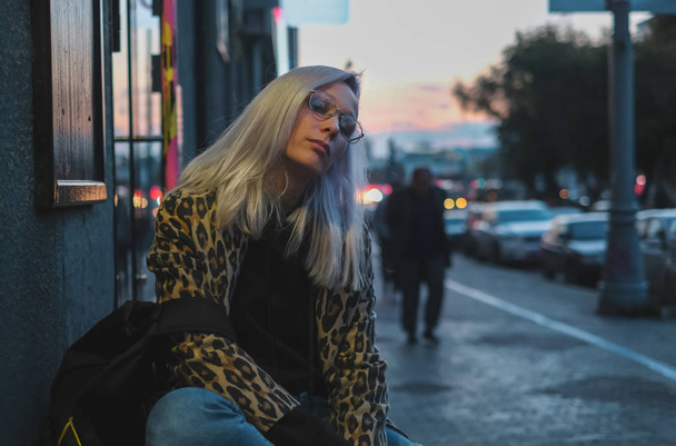 Fashionable blonde girl with glasses in leopard coat at street in the evening - Zdjęcie, obraz