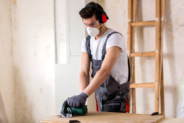 Trabajador joven con una máscara protectora y cortar algunas placas de madera
  - Foto, imagen