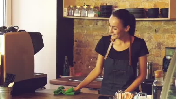 Een aantrekkelijk meisje (de eigenaar van een koffiehuis) veegt een houten tafel. - Video