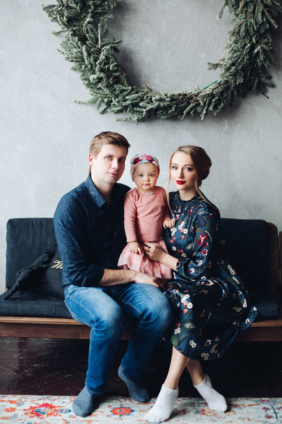 parents and daughter sitting on sofa under big fir wreath. - Photo, Image